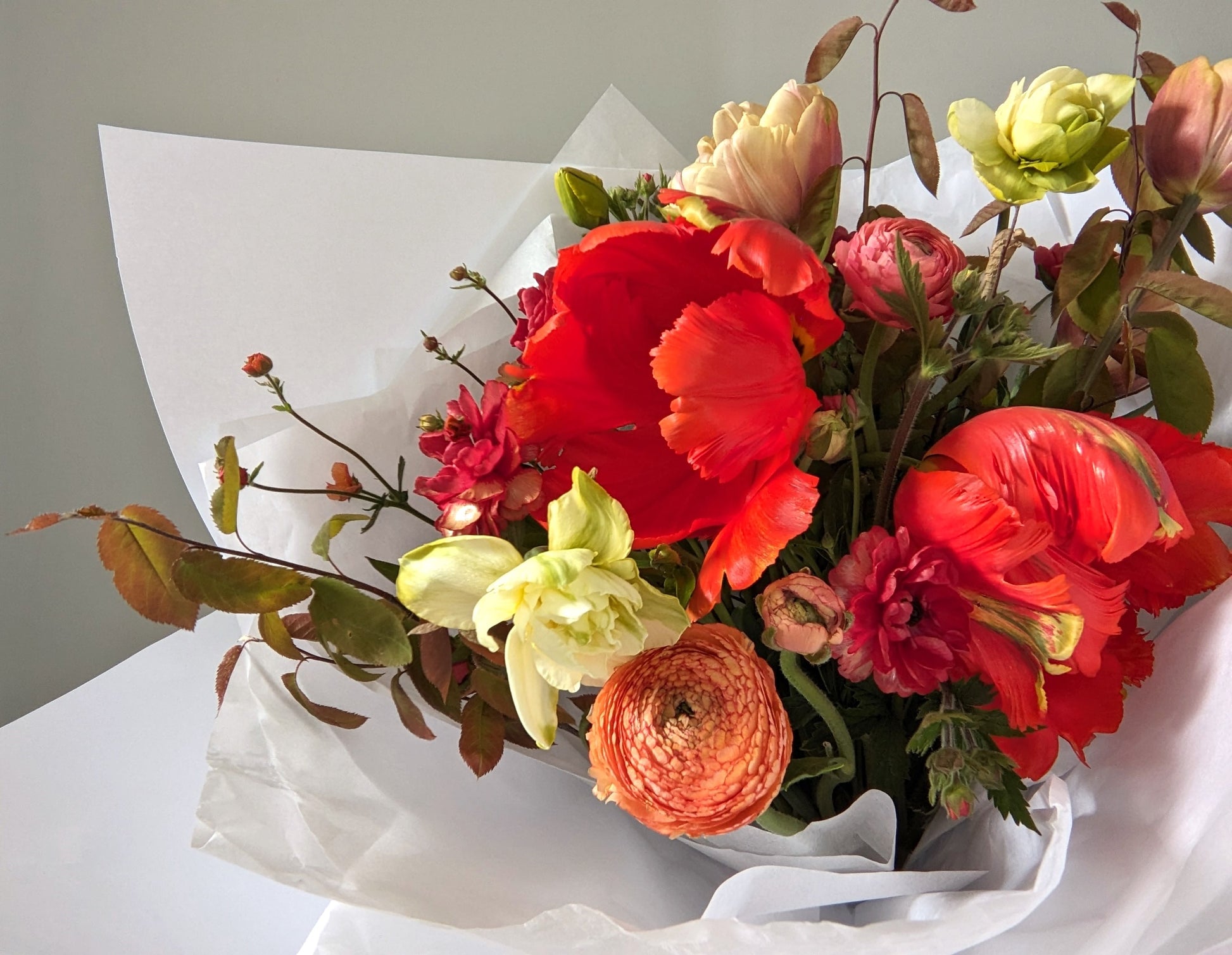 Fresh cut bouquet of bright spring flowers wrapped in white tissue and kraft paper