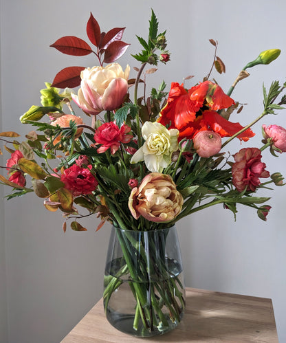 Vase arrangement of British grown flowers and foliage in peach, orange and red